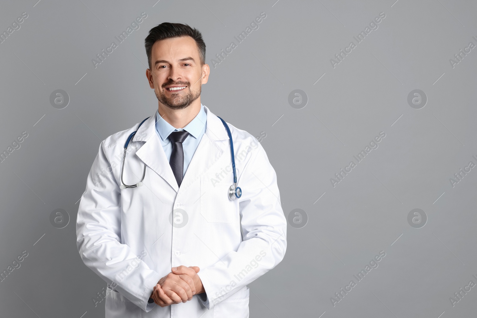 Photo of Smiling doctor with stethoscope on grey background, space for text