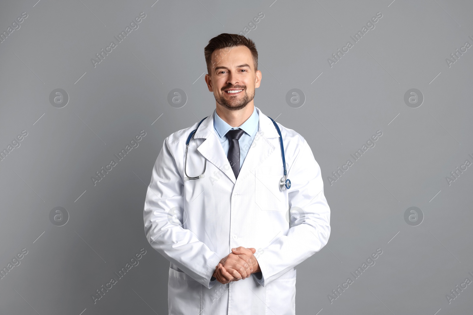 Photo of Smiling doctor with stethoscope on grey background