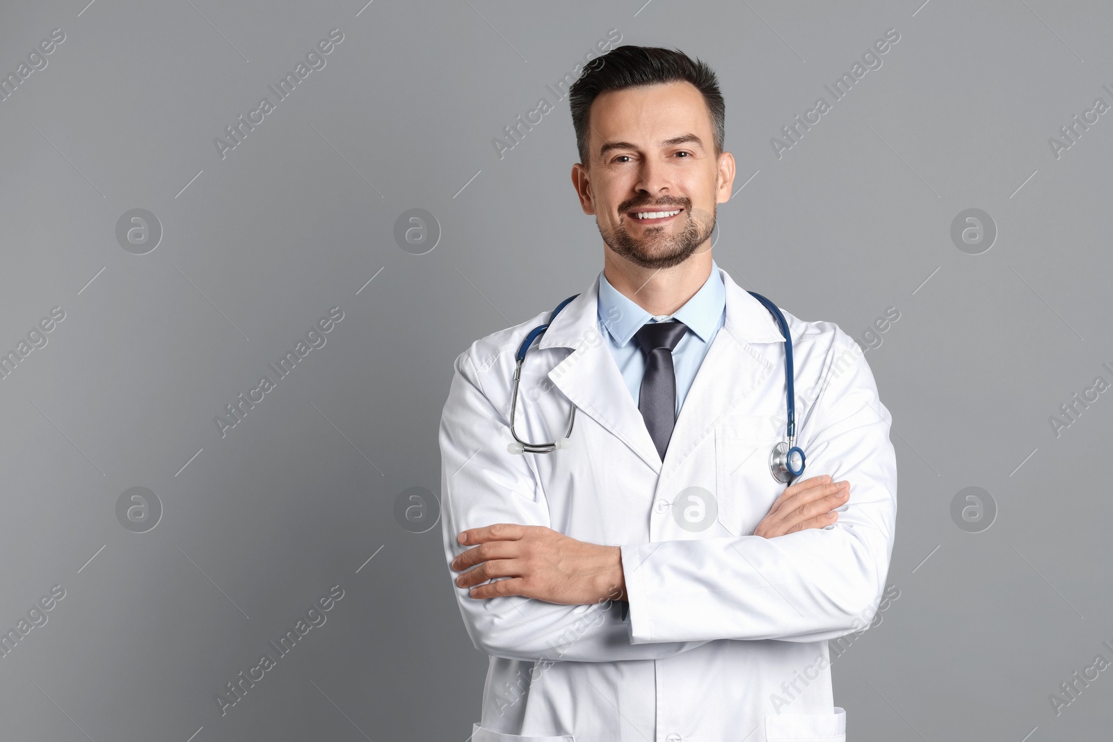 Photo of Smiling doctor with stethoscope on grey background, space for text