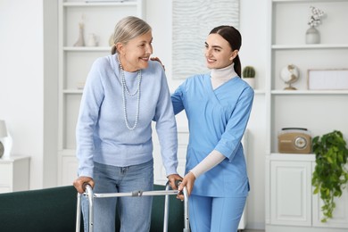 Nurse helping senior woman with walking frame indoors