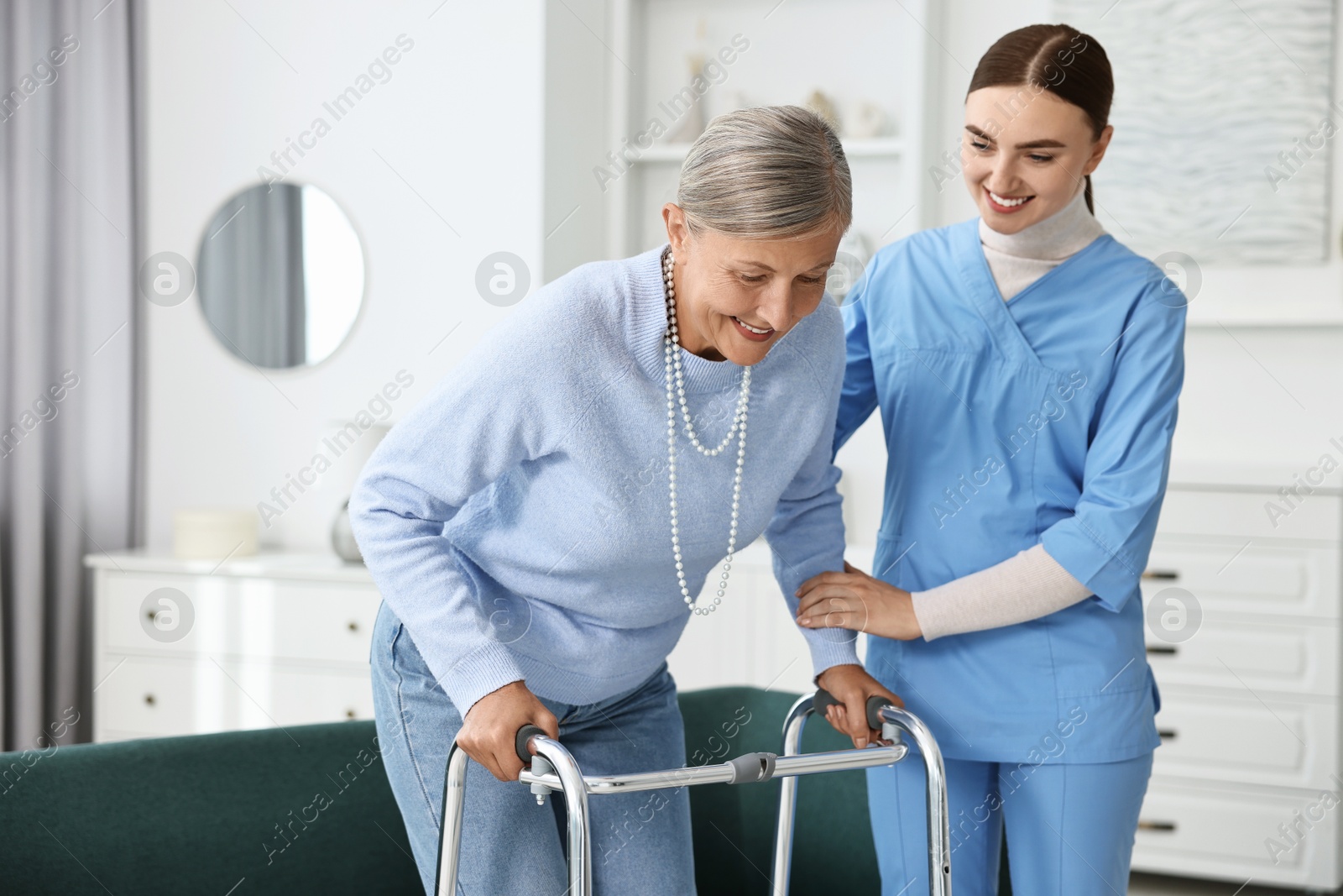 Photo of Nurse helping senior woman with walking frame indoors