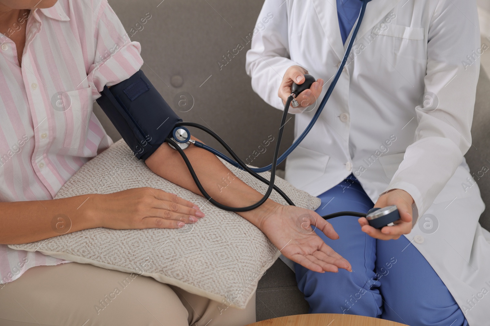 Photo of Doctor measuring patient's blood pressure on sofa indoors, closeup