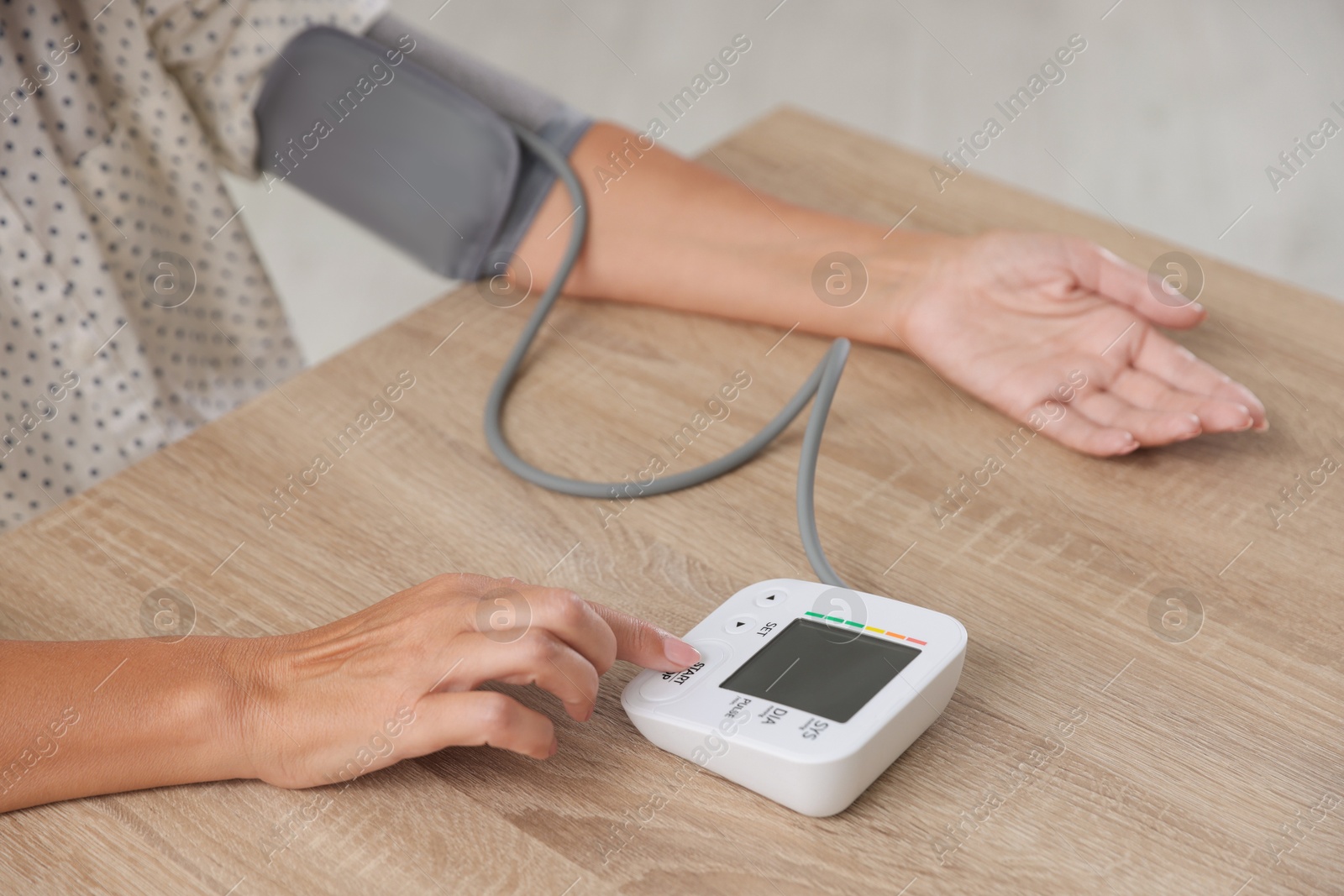 Photo of Woman measuring blood pressure at wooden table indoors, closeup