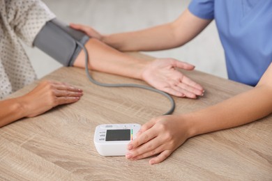 Photo of Healthcare worker measuring patient's blood pressure at wooden table indoors, closeup