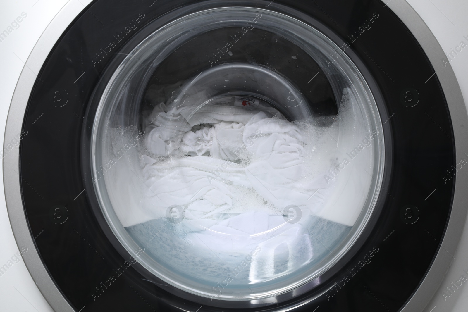 Photo of Washing machine with clothes and suds as background, closeup