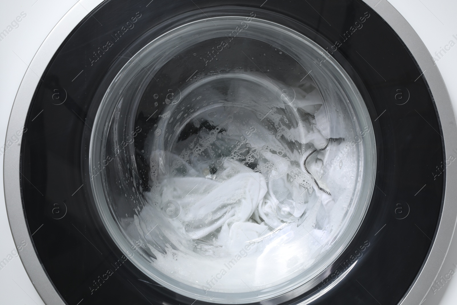 Photo of Washing machine with clothes and suds as background, closeup