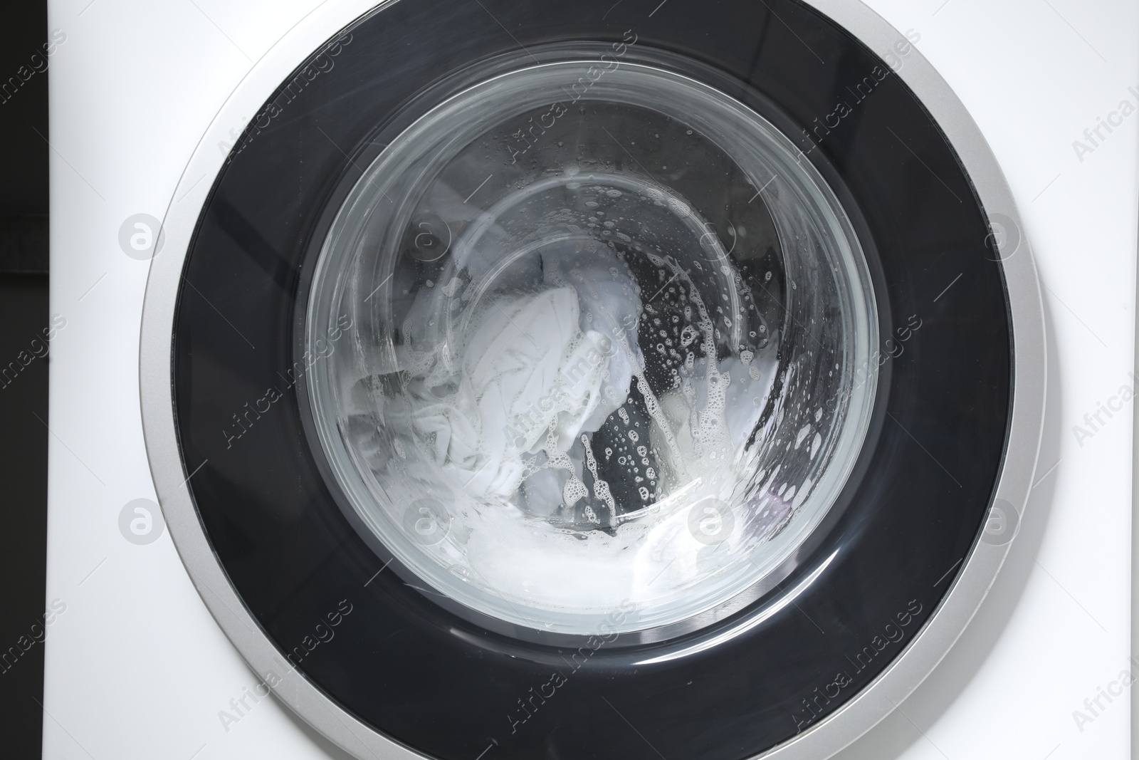 Photo of Washing machine with clothes and suds as background, closeup