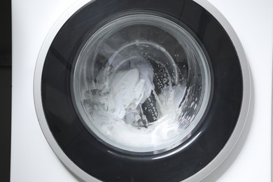 Washing machine with clothes and suds as background, closeup