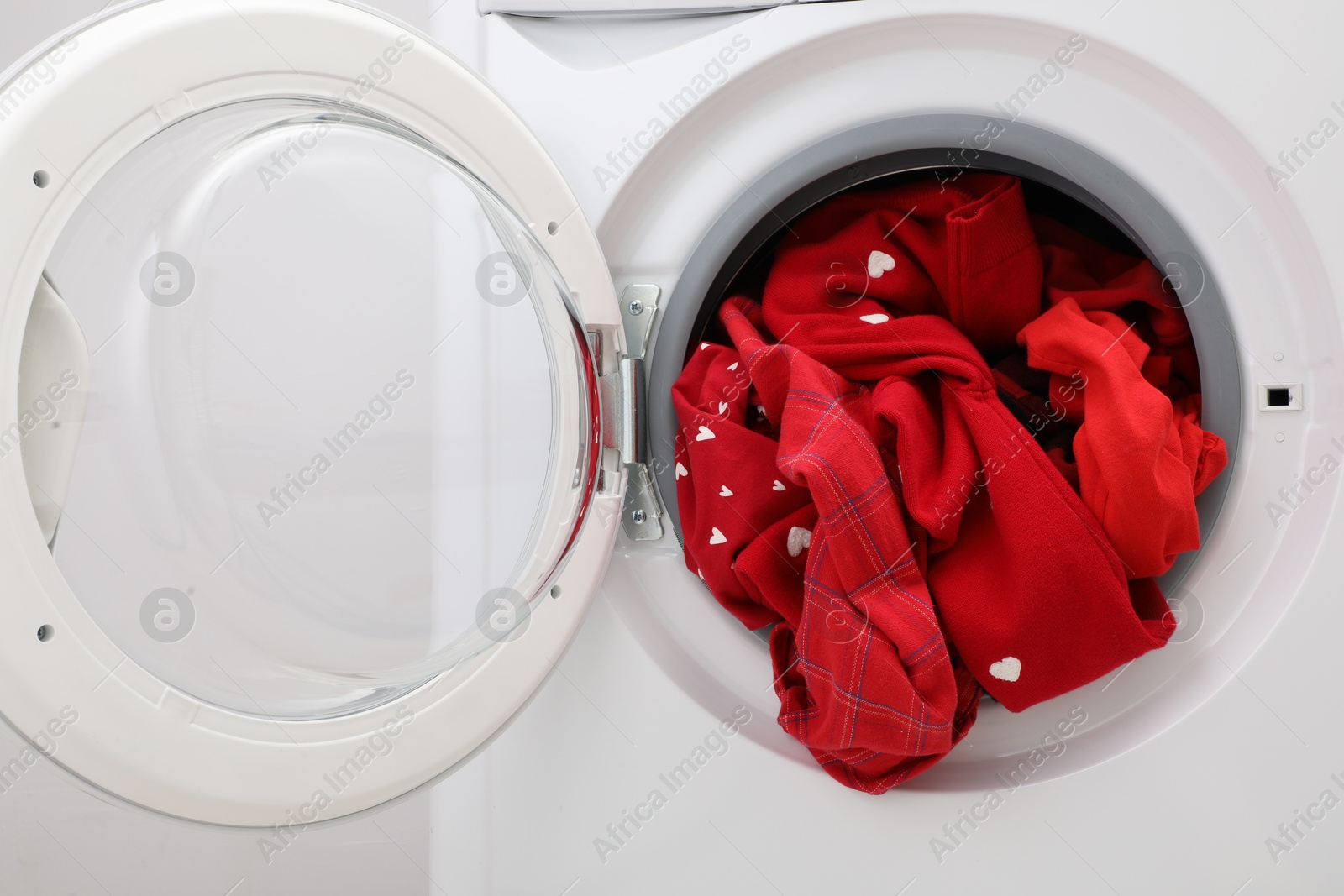 Photo of Washing machine with laundry near light wall, closeup