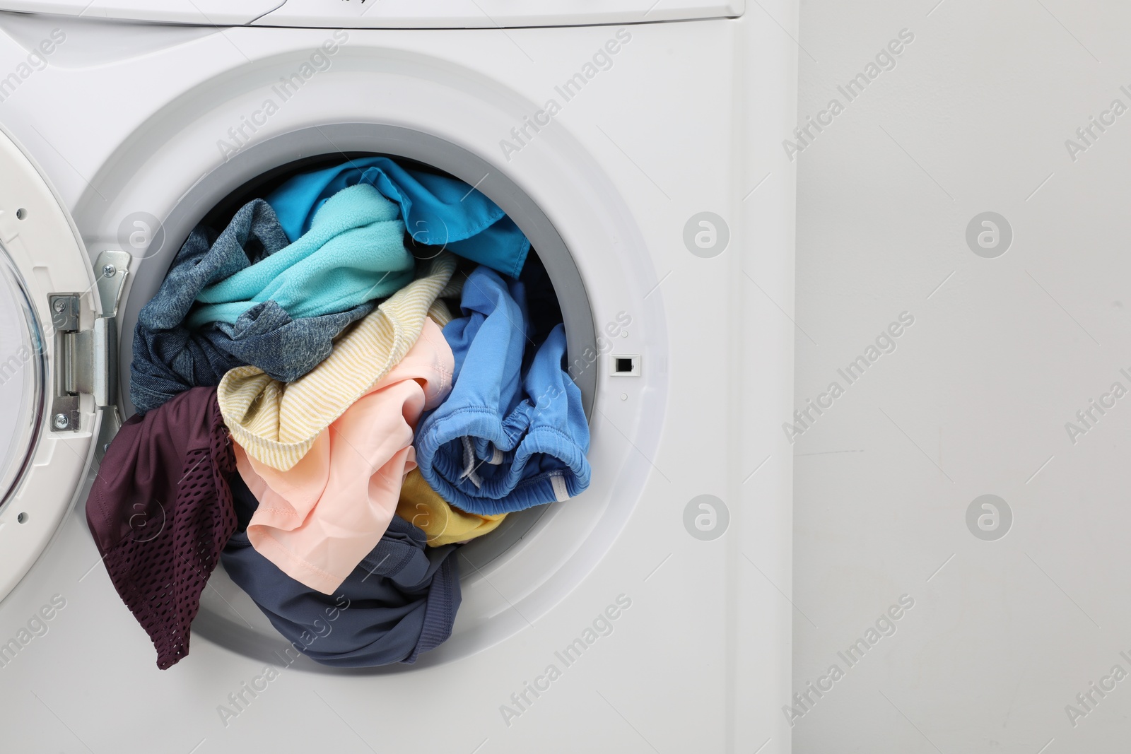 Photo of Washing machine with laundry near light wall, closeup