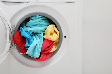 Photo of Washing machine with laundry near light wall, closeup