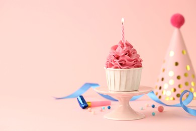 Photo of Tasty cupcake with burning candle and party cone on pink background, space for text