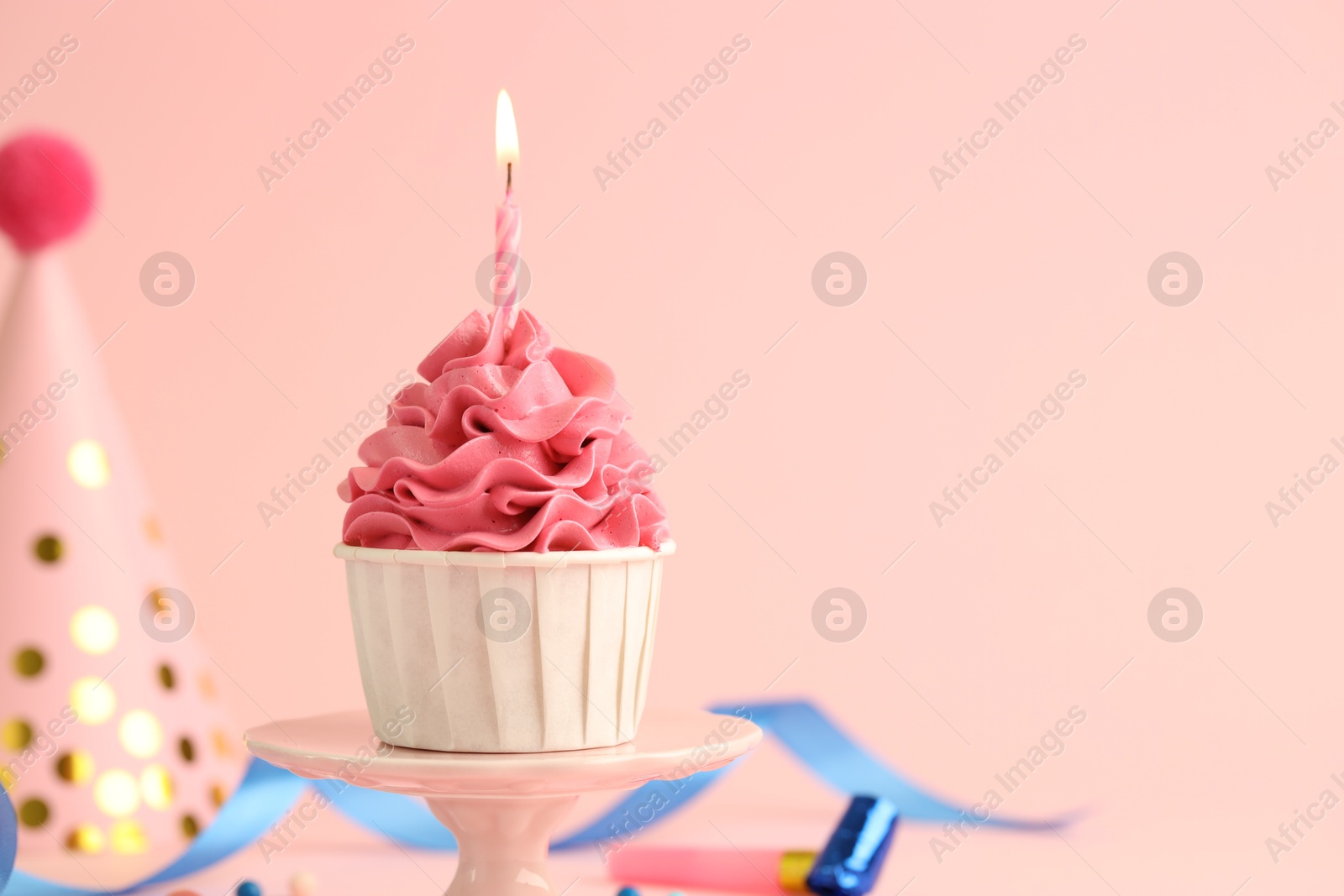 Photo of Tasty cupcake with burning candle and party cone on pink background, space for text