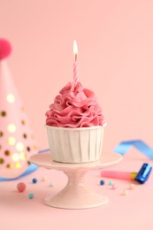 Tasty cupcake with burning candle and party cone on pink background