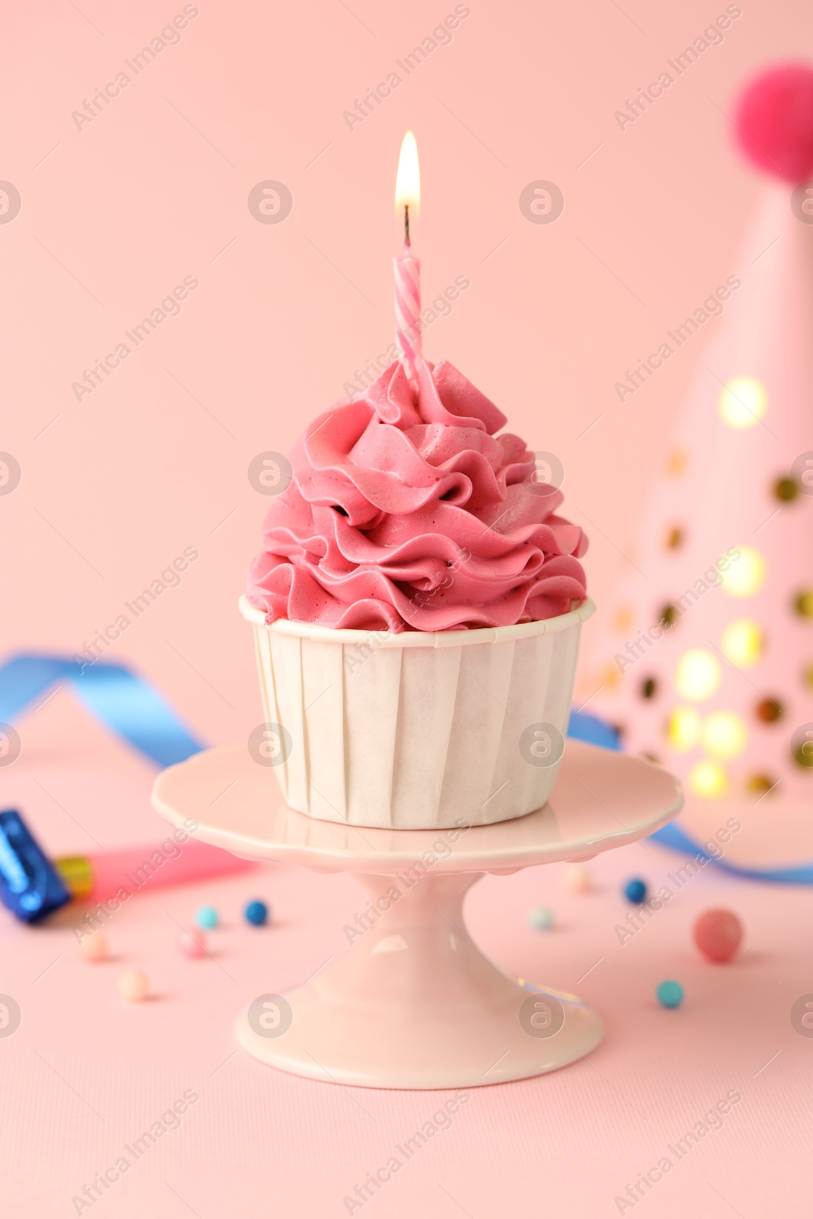 Photo of Tasty cupcake with burning candle and party cone on pink background