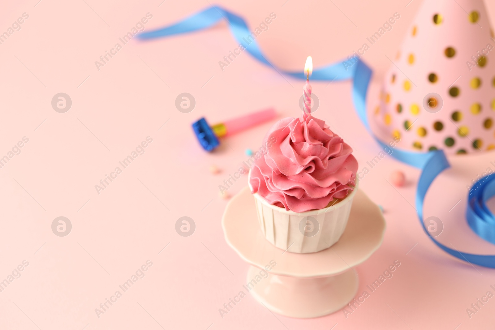 Photo of Tasty cupcake with burning candle and party cone on pink background, space for text