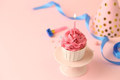 Photo of Tasty cupcake with burning candle and party cone on pink background, space for text