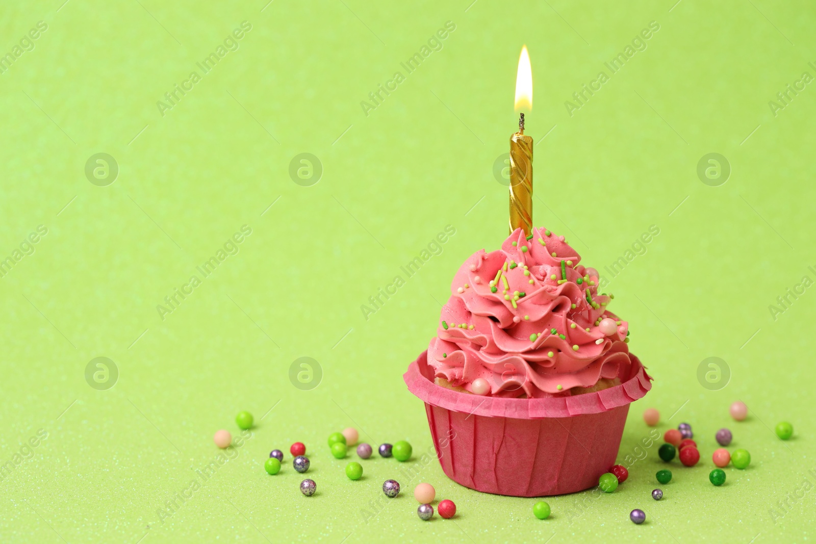 Photo of Tasty cupcake with burning candle on light green background, space for text