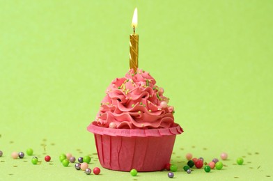 Photo of Tasty cupcake with burning candle on light green background