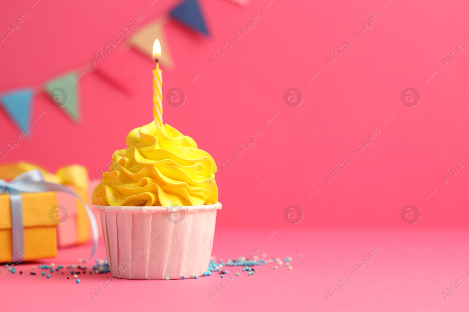 Photo of Tasty cupcake with burning candle and gift boxes on pink background, space for text