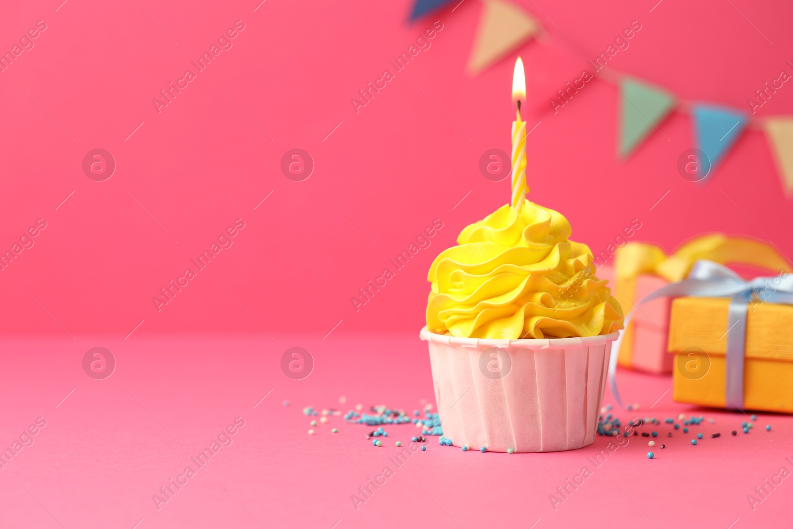 Photo of Tasty cupcake with burning candle and gift boxes on pink background, space for text