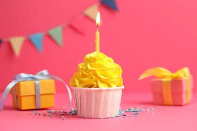 Photo of Tasty cupcake with burning candle and gift boxes on pink background