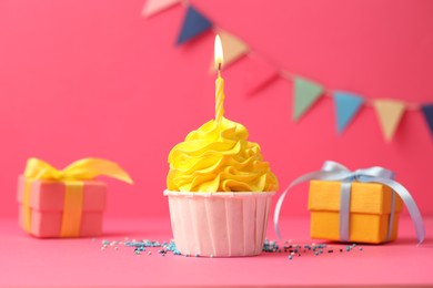 Photo of Tasty cupcake with burning candle and gift boxes on pink background