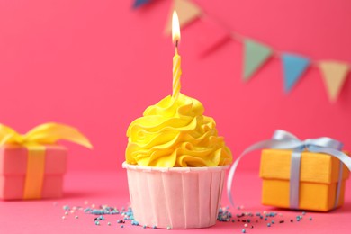 Photo of Tasty cupcake with burning candle and gift boxes on pink background