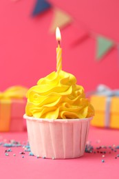 Photo of Tasty cupcake with burning candle and gift boxes on pink background