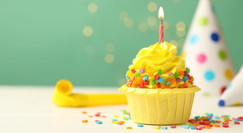 Photo of Tasty cupcake with burning candle and party cones on green background with blurred lights, space for text