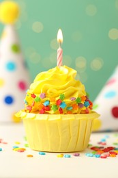 Photo of Tasty cupcake with burning candle and party cones on green background with blurred lights