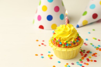 Photo of Tasty cupcake with burning candle and party cones on white table, space for text