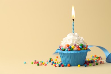 Photo of Tasty cupcake with burning candle on beige background, space for text