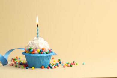 Photo of Tasty cupcake with burning candle on beige background, space for text