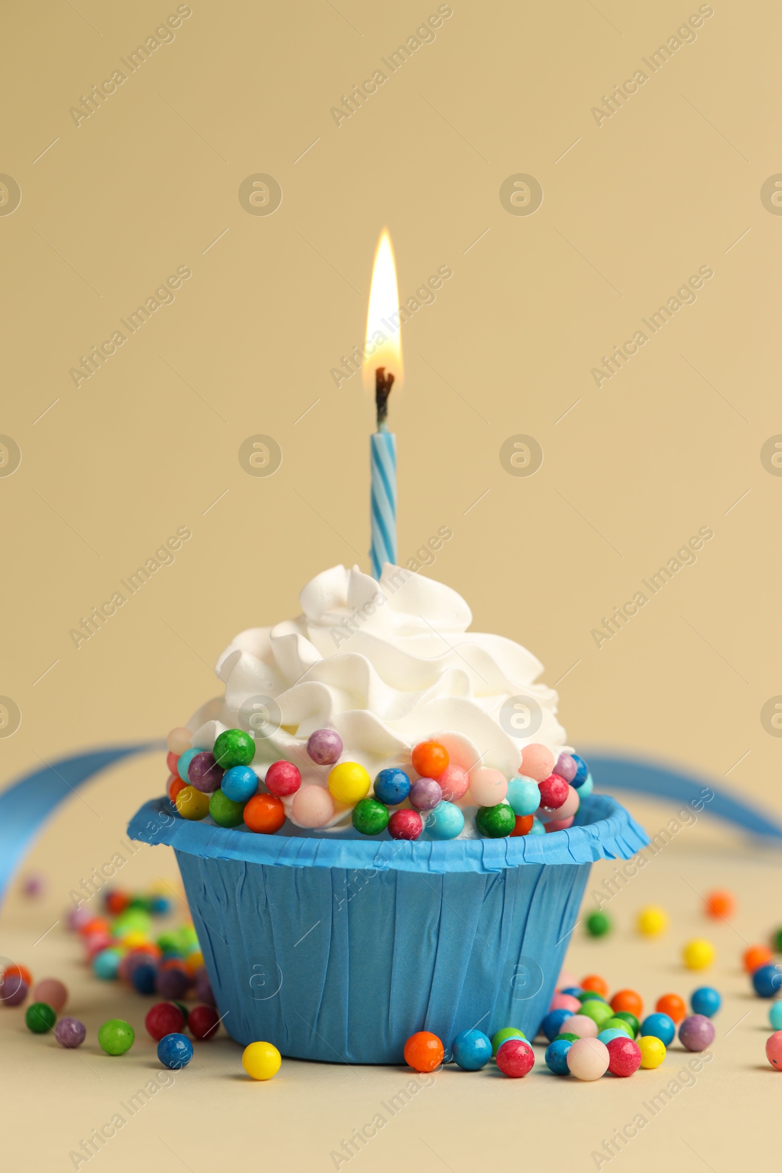 Photo of Tasty cupcake with burning candle on beige background