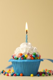 Photo of Tasty cupcake with burning candle on beige background