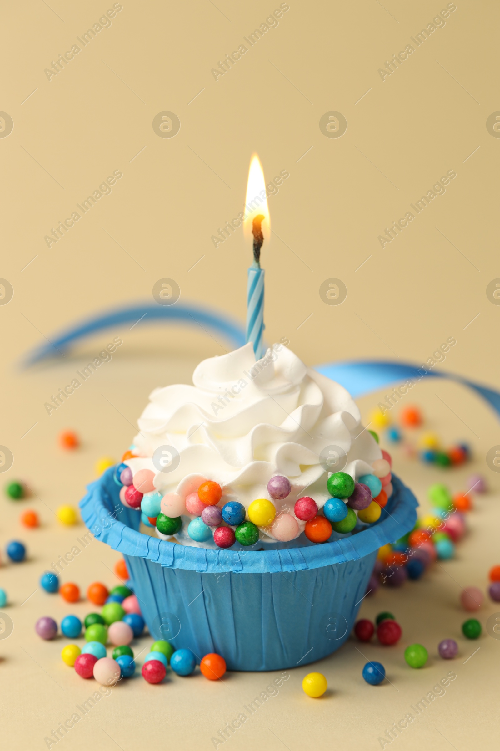 Photo of Tasty cupcake with burning candle on beige background