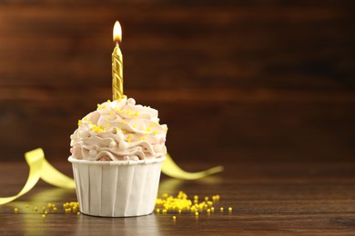 Photo of Tasty cupcake with burning candle on wooden table, space for text