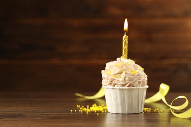 Photo of Tasty cupcake with burning candle on wooden table, space for text