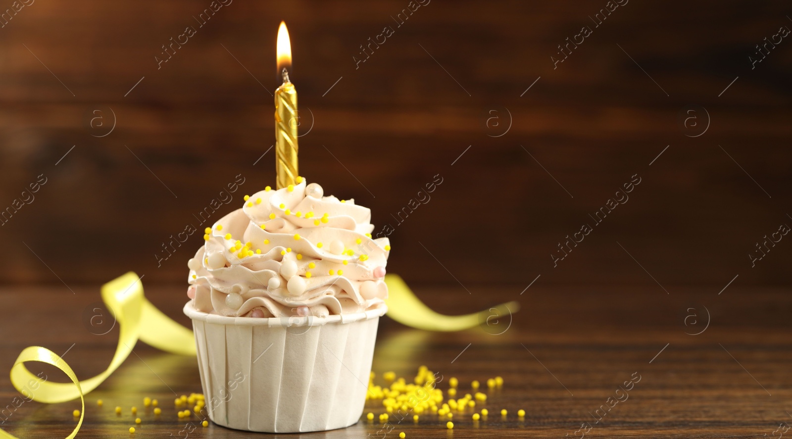 Photo of Tasty cupcake with burning candle on wooden table, space for text