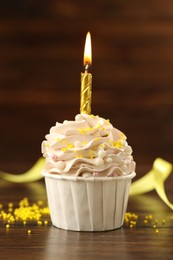 Photo of Tasty cupcake with burning candle on wooden table