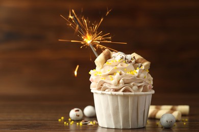 Photo of Tasty cupcake with burning sparkler on wooden table, space for text