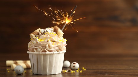 Photo of Tasty cupcake with burning sparkler on wooden table, space for text