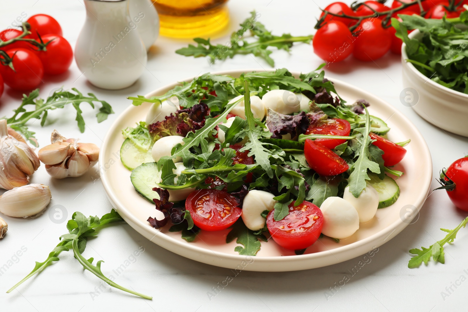 Photo of Tasty salad with arugula, lettuce, mozzarella cheese and vegetables on white table, closeup