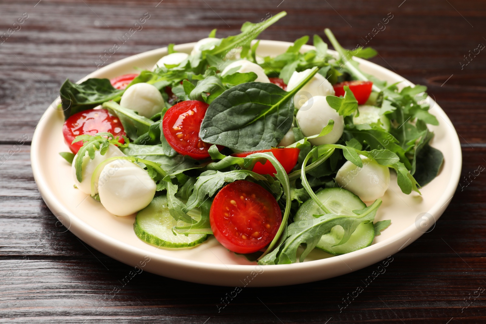 Photo of Tasty salad with arugula, spinach, mozzarella cheese and vegetables on wooden table, closeup