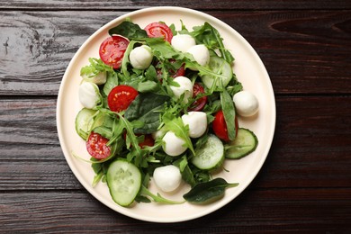 Photo of Tasty salad with arugula, spinach, mozzarella cheese and vegetables on wooden table, top view