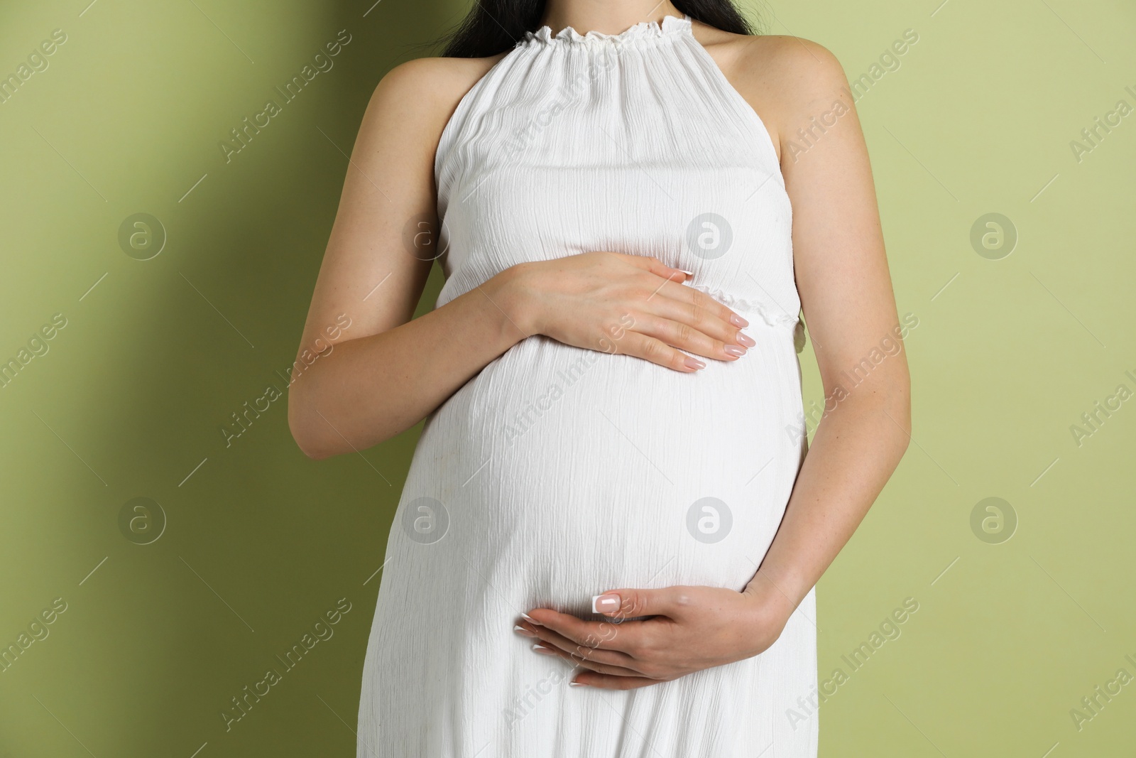 Photo of Young pregnant woman on light olive background, closeup