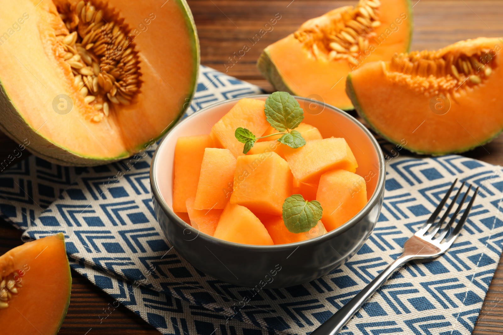 Photo of Pieces of ripe Cantaloupe melon in bowl and fork on table, closeup