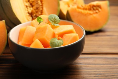 Photo of Pieces of Cantaloupe melon and mint in bowl on wooden table, closeup