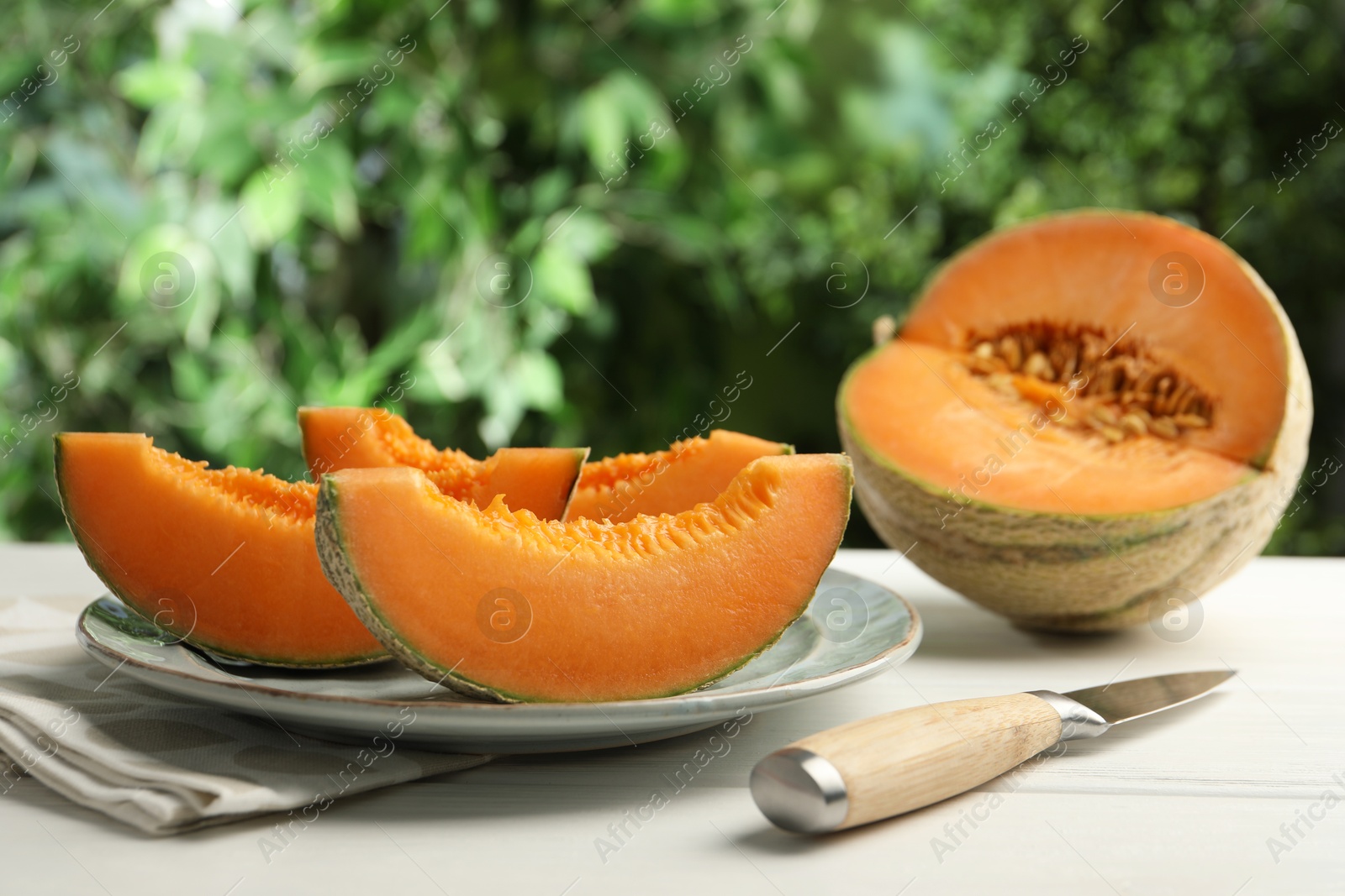 Photo of Pieces of fresh Cantaloupe melon and knife on white wooden table, closeup